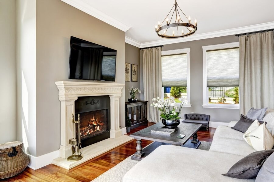 A living room space with a TV mounted above a fireplace, a couch, and two windows featuring two motorized shades lowered halfway.