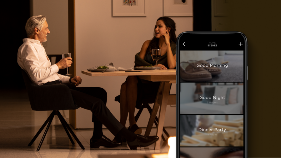 A couple having dinner in a warmly illuminated space while the Savant app displays different scenes 