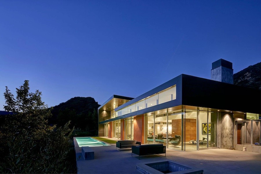 outside view of a home with interior lights all turned on inside and a pool and seating area outside